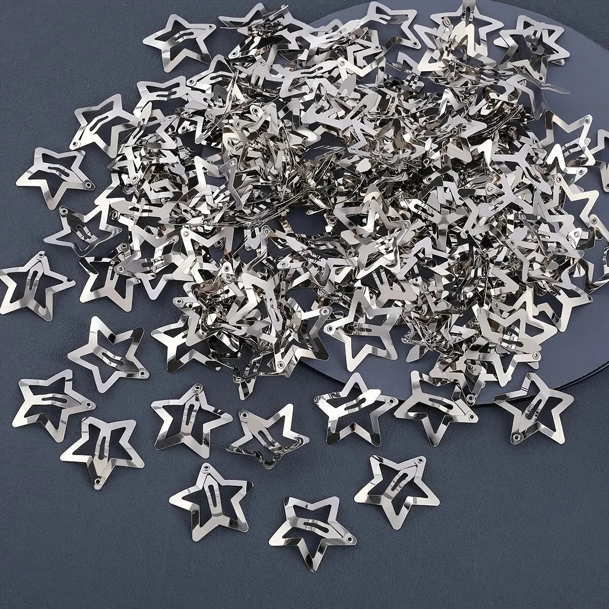 A pile of silver star metal snap hair clips scattered on a dark surface.