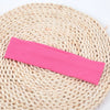 A bright pink knitted elastic headband lying on a natural woven mat.