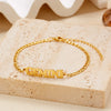 Gold stainless steel zodiac constellation charm bracelet resting on a light beige stone surface.