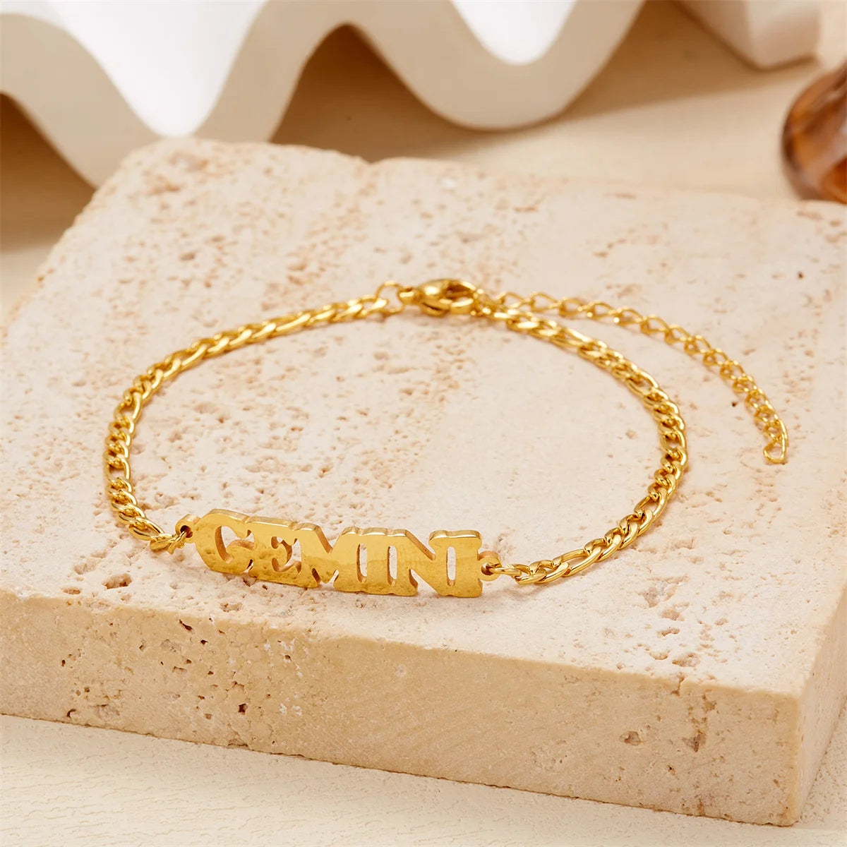 Gold stainless steel zodiac constellation charm bracelet resting on a light beige stone surface.