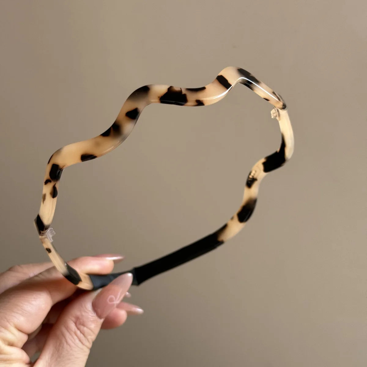 Una mano sostiene unos aretes de cabello ondulado de acetato color tortuga contra un fondo neutro.