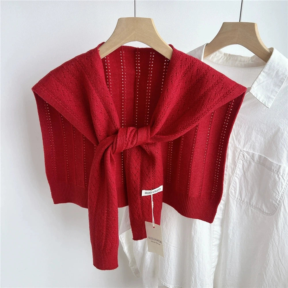 Un chal o prenda exterior de acrílico tejido rojo doblado, exhibido en un perchero blanco.