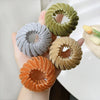A hand holds three elegant horsetail hair clips in shades of gray, olive green, and copper.
