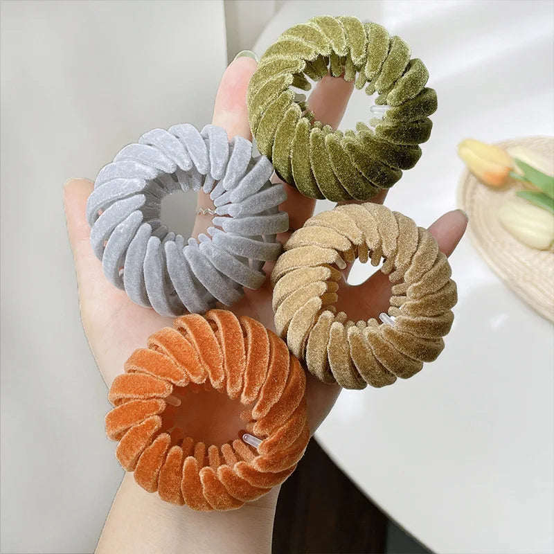 A hand holds three elegant horsetail hair clips in shades of gray, olive green, and copper.