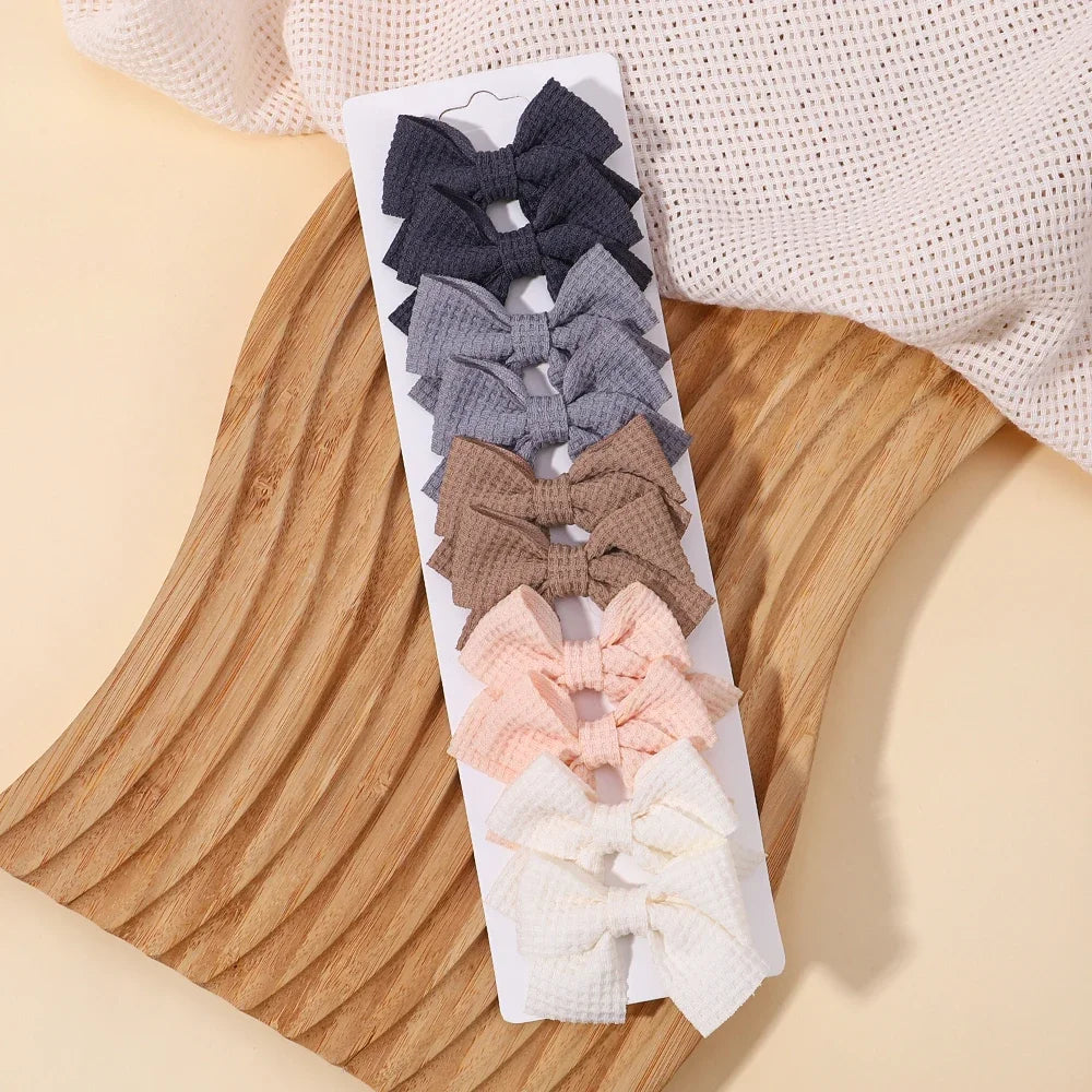 A display of pink, gray, and brown handmade ribbon bow hair clips arranged on a white card against a light background.
