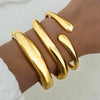 A set of three gold geometric wave bangles worn on a wrist.