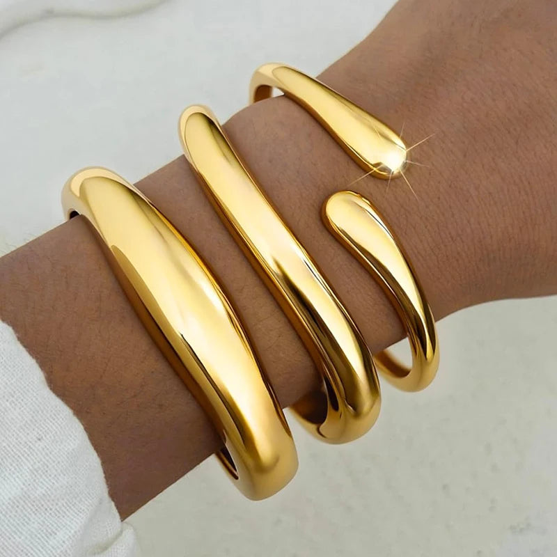 A set of three gold geometric wave bangles worn on a wrist.