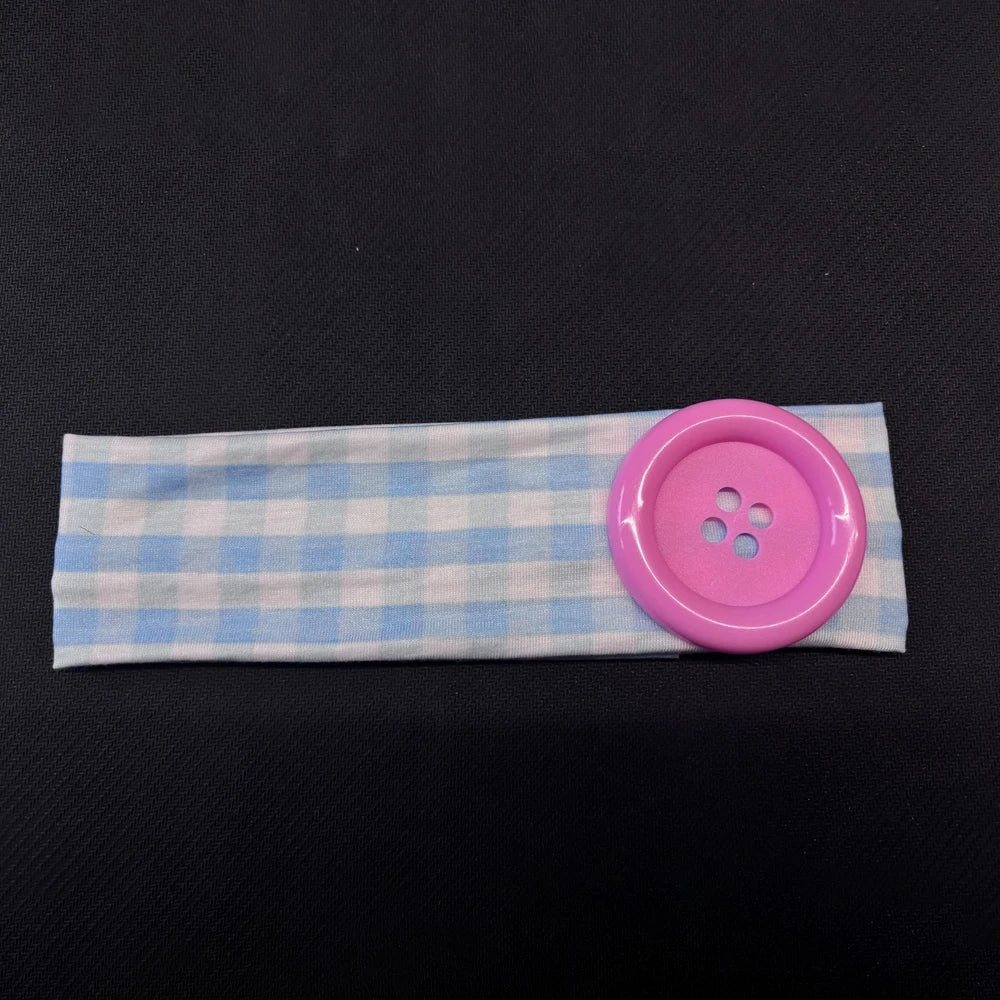 A light blue and white plaid fabric headband with a pink button attached.