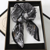 A black and white patterned silk scarf tied in a bow displayed in a wooden frame.