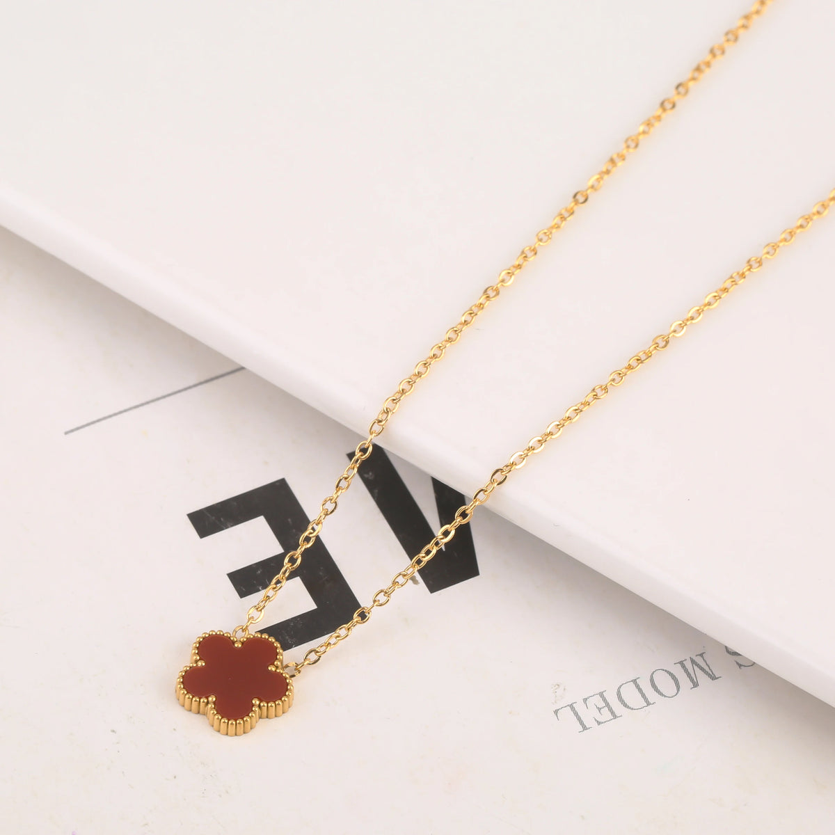 Pulsera de flor de planta de acero inoxidable chapado en oro con un dije marrón rojizo sobre fondo blanco.