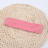 A pink knitted elastic headband lying on a natural woven mat.