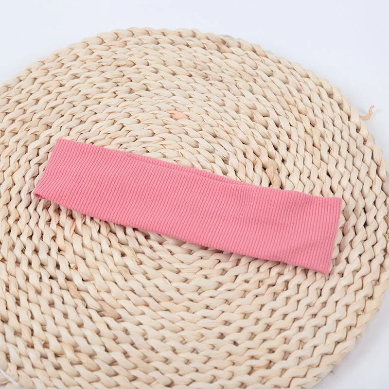 A pink knitted elastic headband lying on a natural woven mat.