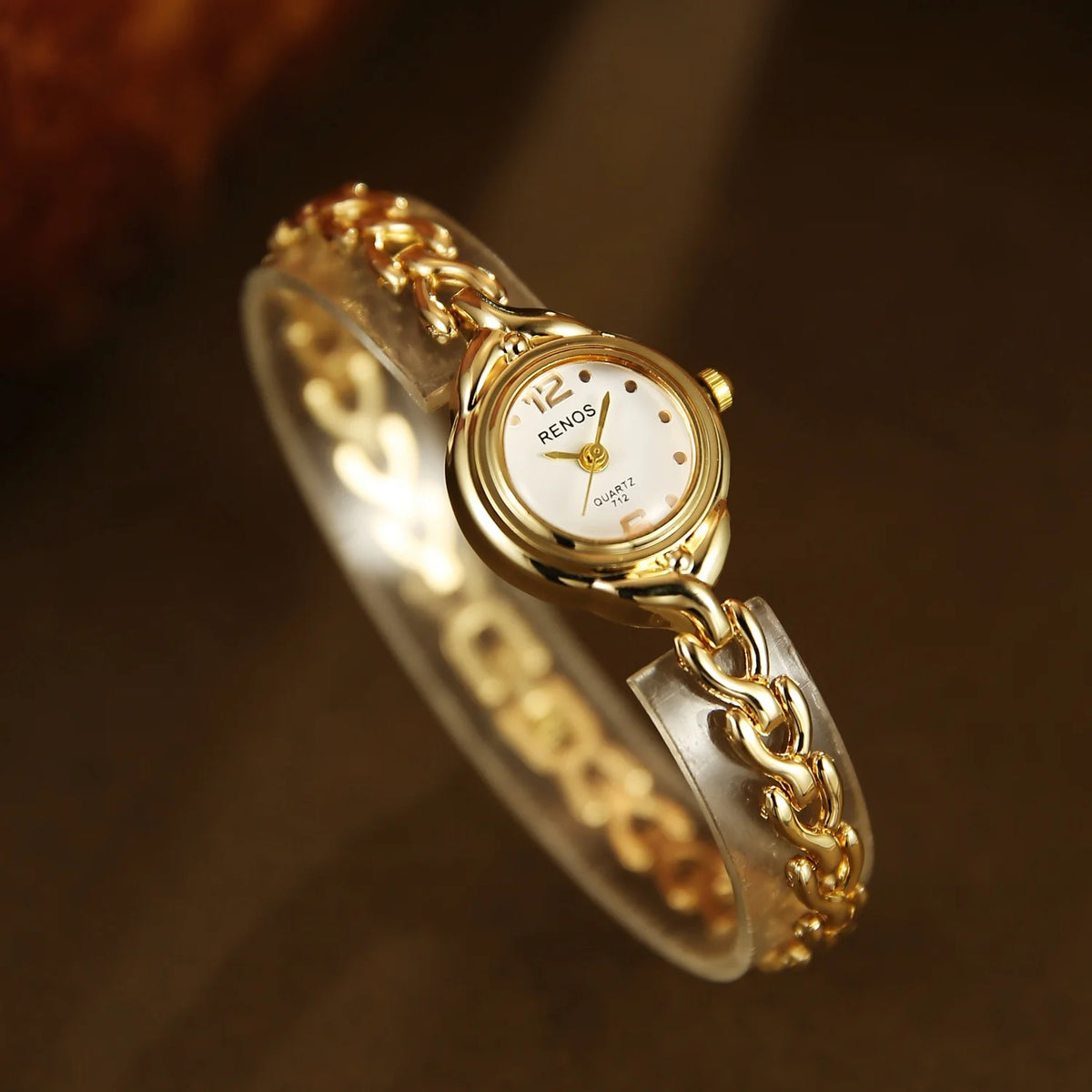 A gold-toned quartz wristwatch with a clear strap and gold chain link bracelet on a dark background.