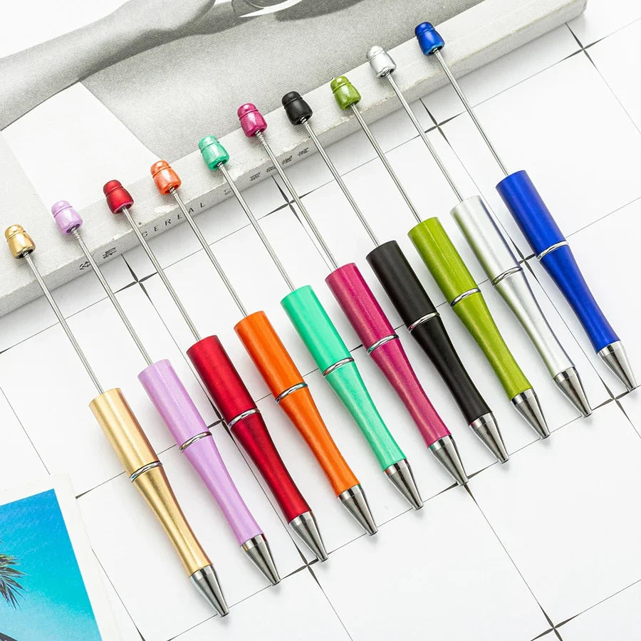 A collection of ten colorful beadable ballpoint pens arranged diagonally on a white surface.