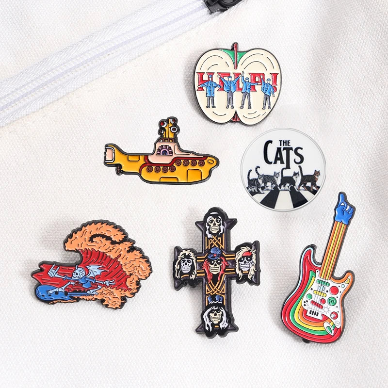 Collection de pins en émail représentant un sous-marin jaune, une silhouette de chat et une forme de guitare sur fond blanc.