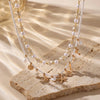 A delicate gold and white beaded necklace featuring starfish and shell charms displayed on a light stone.