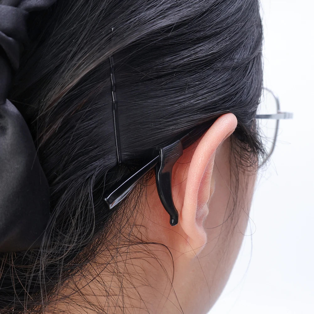 A close-up of a person's dark hair with silicone anti-slip ear hooks attached to the back of the ear.