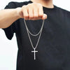 Una mano sostiene un collar de cruz de acero inoxidable plateado contra una camiseta negra.