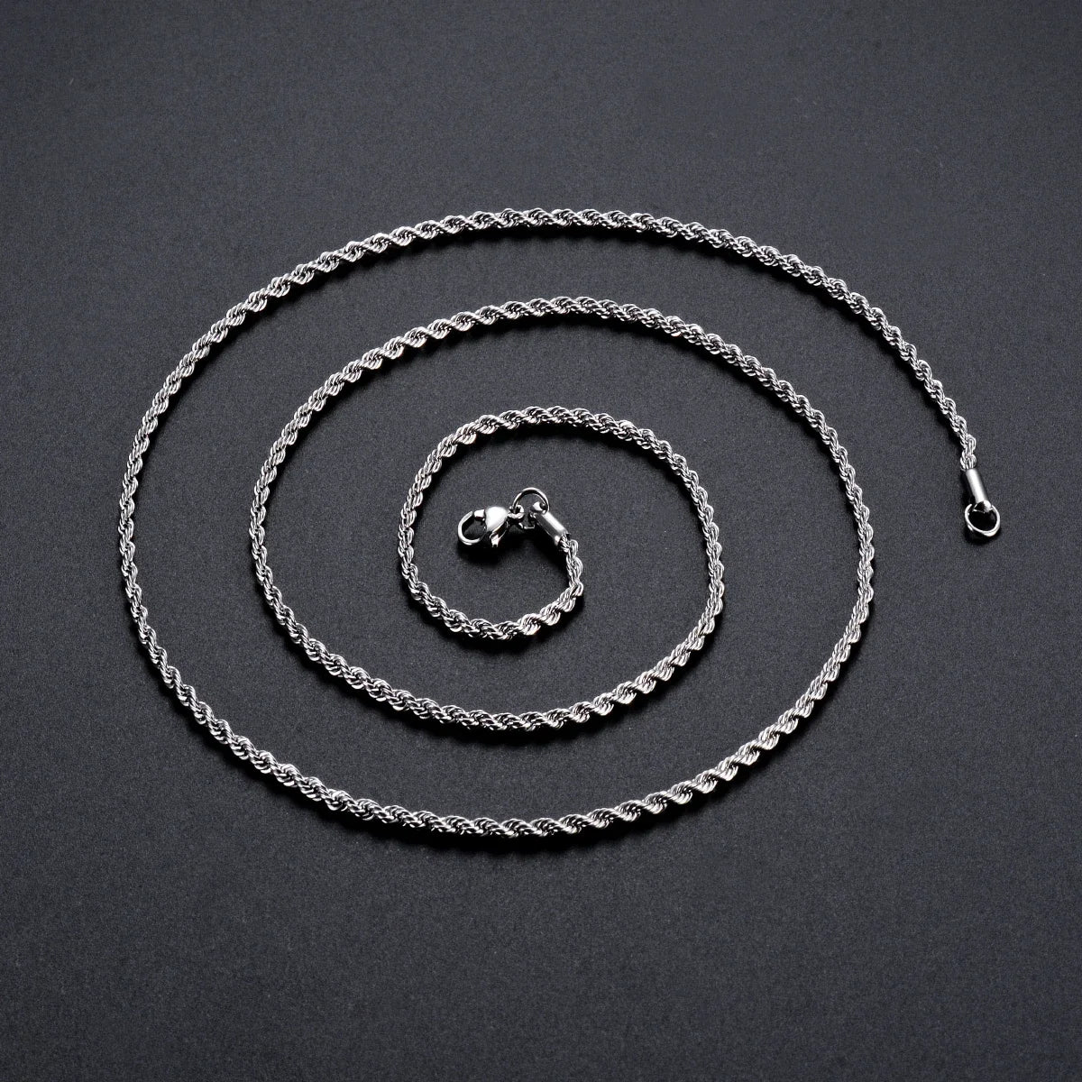 Collar de cadena de cuerda plateada enrollado sobre una superficie oscura.