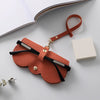 An orange leather pouch with a strap is shown next to a white box on a light gray surface.