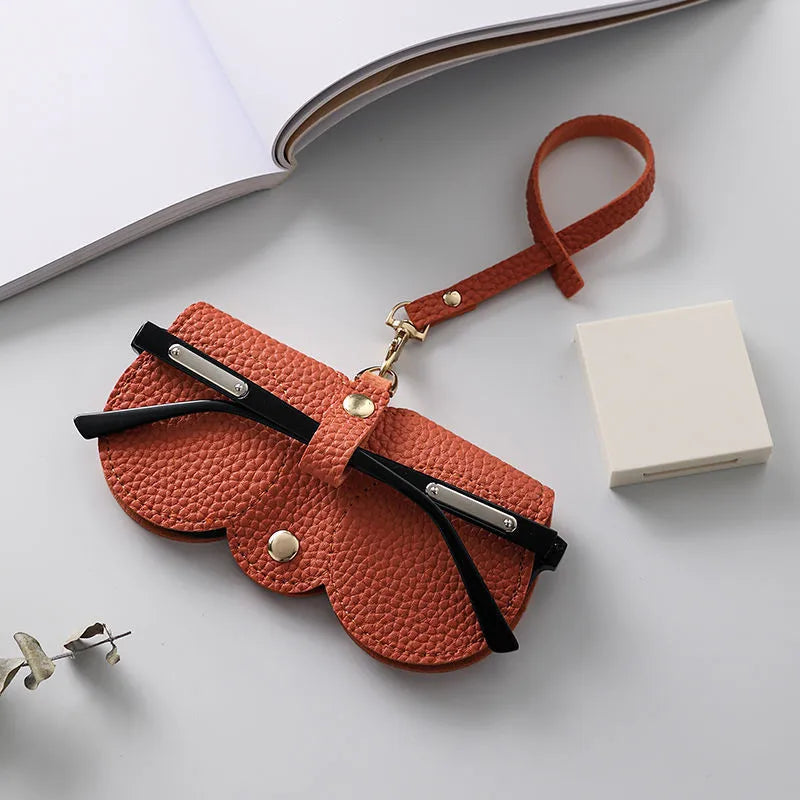 An orange leather pouch with a strap is shown next to a white box on a light gray surface.