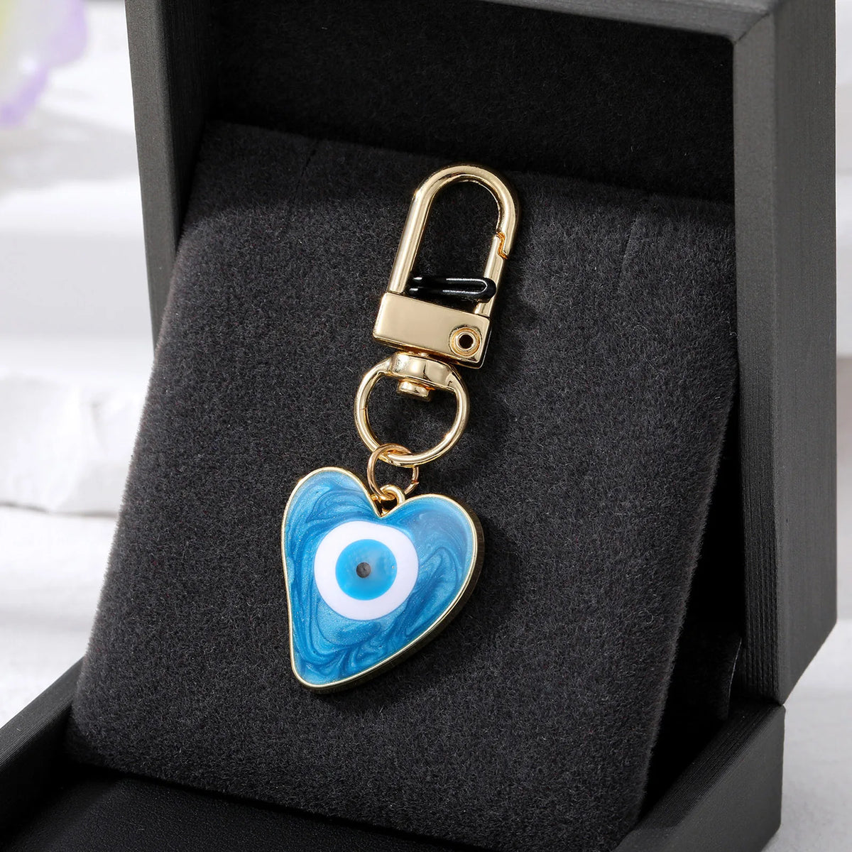 A gold-colored heart keychain featuring a blue and white Turkish Evil Eye design, displayed in a black velvet box.