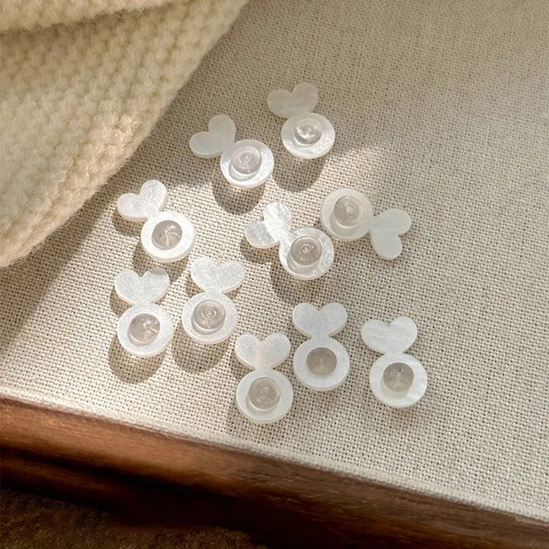 A collection of clear, heart-shaped and round silicone earring lifters for studs jewelry making placed on a light fabric surf