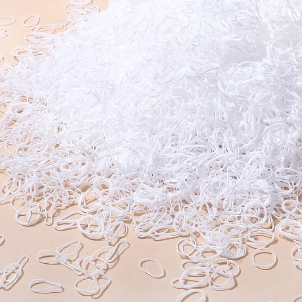 A pile of white disposable rubber hair ties for kids scattered on a light surface.
