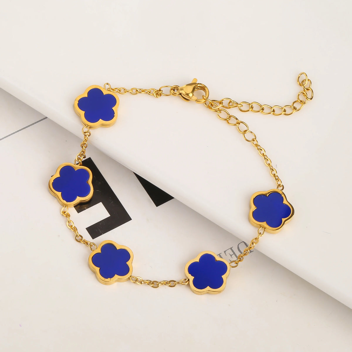 Pulsera de acero inoxidable chapada en oro con pequeños charms de flores azules en una cadena dorada.