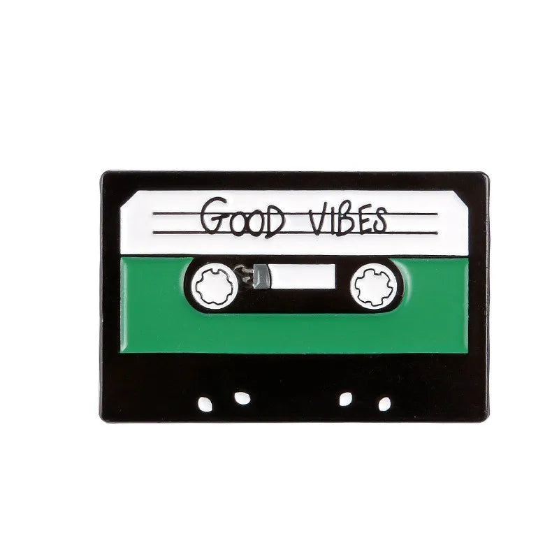 A black enamel pin featuring the text Good Vibes on a white background with green accents.