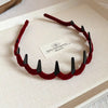 A maroon resin wave toothed headband for women displayed on a light-colored box.
