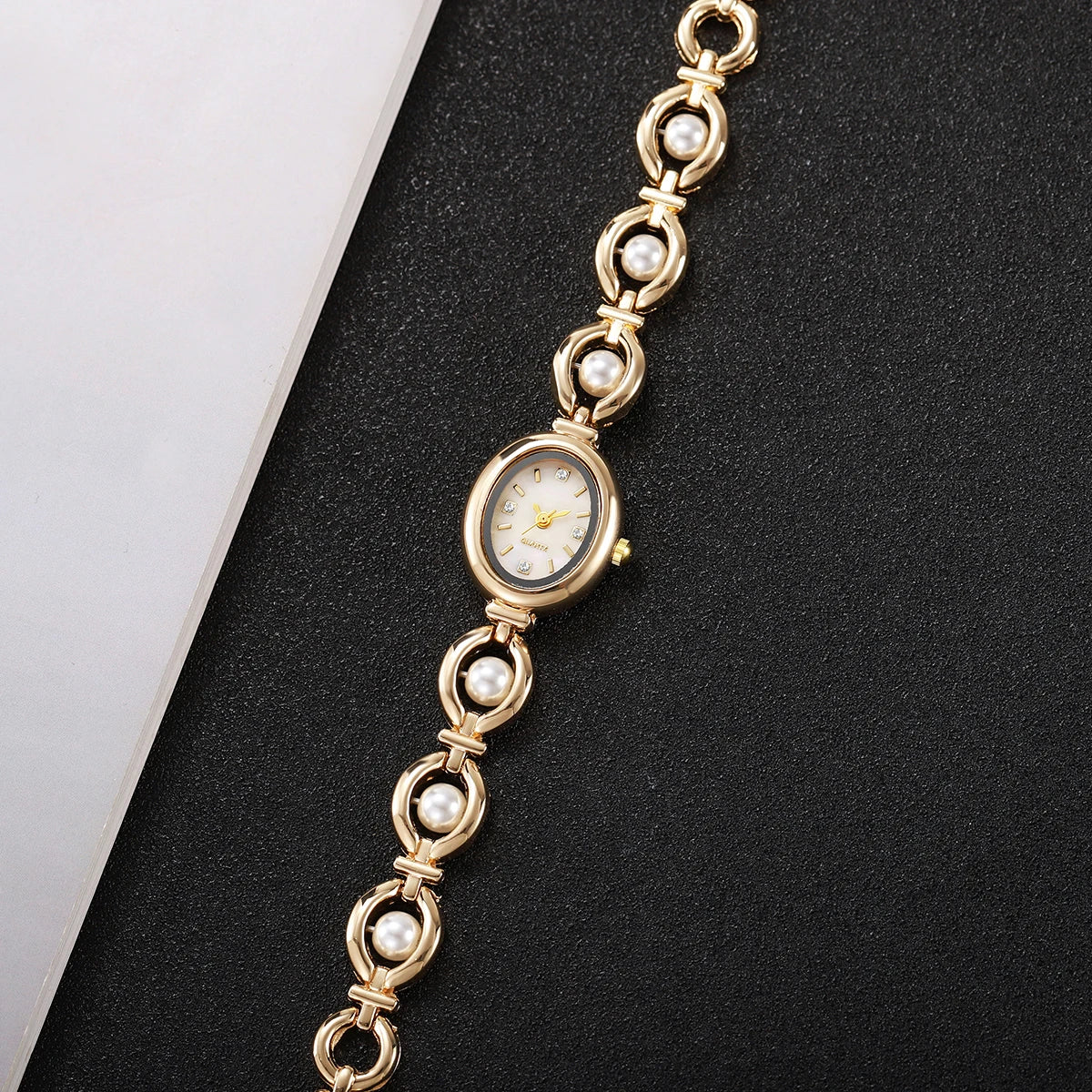 Eleganße Perlmutt-Quarz-Armbanduhr in Goldton mit feinem Kettenglied, vor schwarzem Hintergrund.