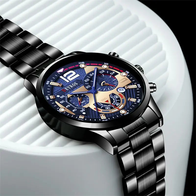 A close-up shot of a black stainless steel quartz watch with a blue dial and gold accents resting on a white surface.
