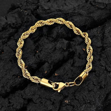 A gold-colored stainless steel twisted chain bracelet laid on a dark, textured surface.