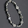 Rosario de brazalete gris oscuro con medallas plateadas y una cruz en cadena de cuentas negras.