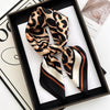 A luxury leopard print silk scarf tied in a bow displayed in a black frame.