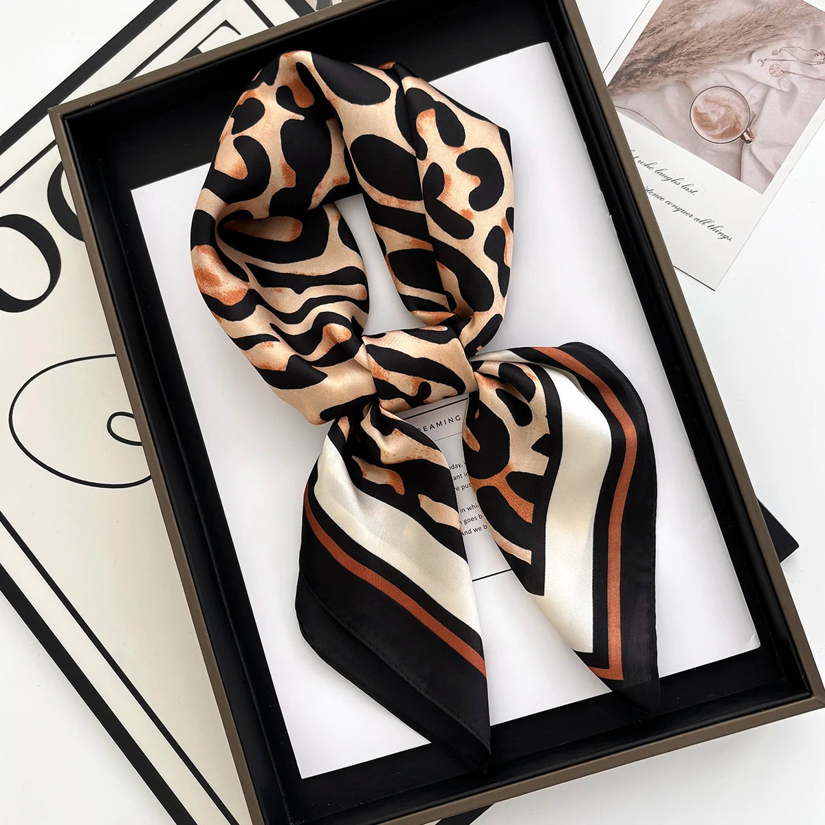A luxury leopard print silk scarf tied in a bow displayed in a black frame.