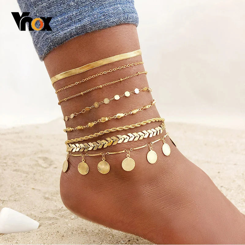 A close-up of multiple layered gold stainless steel anklets worn on a person's foot.
