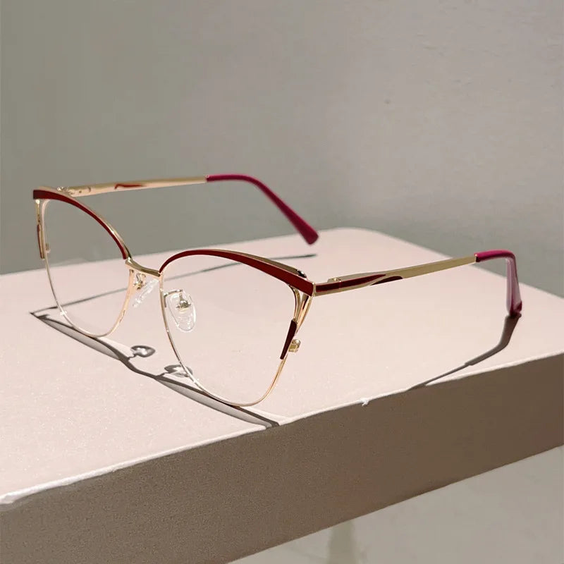 Un par de gafas de computadora con diseño de gato y marco de oro rosa con detalles rosas sobre una superficie blanca.