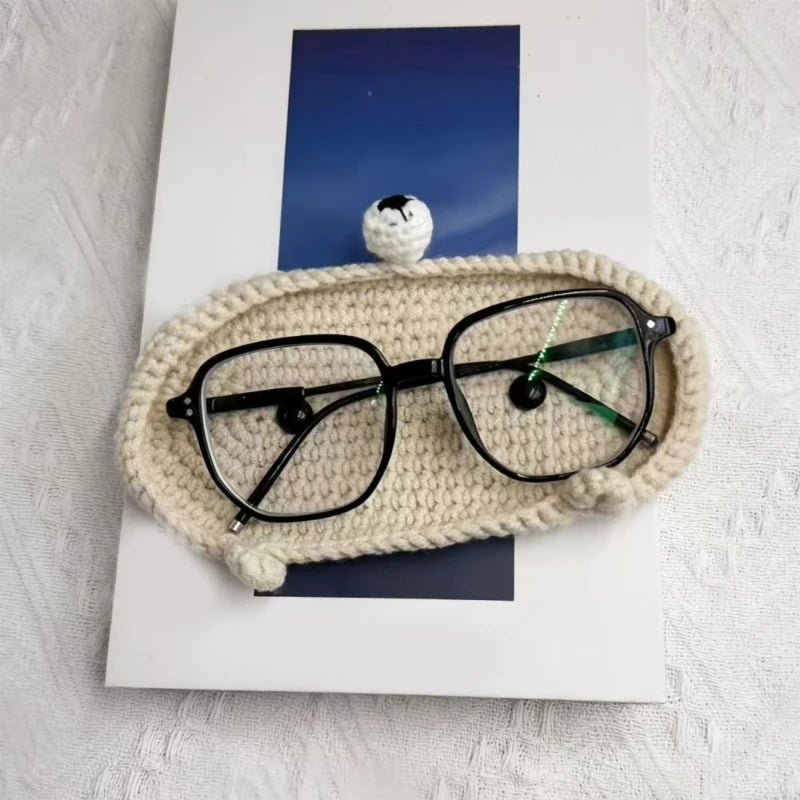 A pair of black eyeglasses rests inside a cream-colored handmade crochet animal storage case.