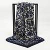 A dark blue and cream patterned silk scarf draped on a black display stand.