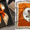 An orange silk scarf with a white floral print is displayed on a dark wooden frame.
