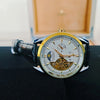 A close-up shot of a gold-toned luxury automatic mechanical men's wristwatch with a dark strap, resting on a black surface.