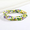 Una pulsera de cuentas de colores, incluyendo púrpura, verde y blanco, dispuesta sobre una superficie blanca.