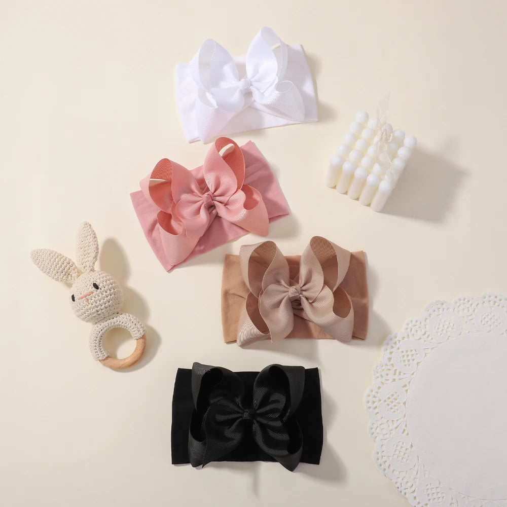 A collection of soft baby headbands featuring chunky hair bows in pink, beige, and black.