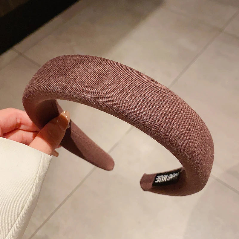 Gros plan d'un bandeau pour cheveux épaissi de couleur café tenu par une main.