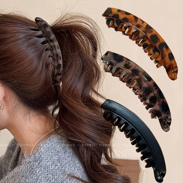 A set of tortoiseshell banana hair clips and a hairpin being used to style long brown hair.