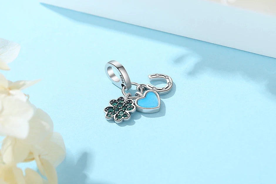 A silver family tree charm necklace featuring a heart pendant and a floral charm on a light blue background.