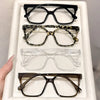 A display of four pairs of elegant geometric reading glasses with various frames and transparent lenses.