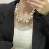 A close-up of an elegant simulated pearl choker necklace worn by a person, displayed against a white top and black blazer.